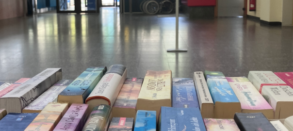 Beim Bücherflohmarkt stehen Bücherreihen stehen in einer großen Halle mit Stinboden