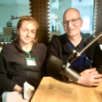 Zwei Beschäftigte der Krankenhaus-Hygiene im Klinikum Solingen sitzen in Dienstkleidung an einem Studiotisch mit Mikro im Vordergrund